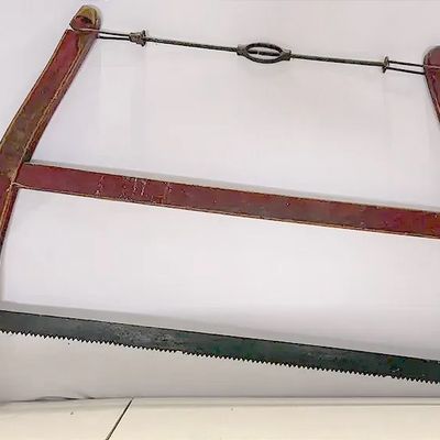 Antique antique buck saw with a red-painted wooden frame and metal tension rod.