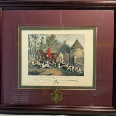 Framed vintage fox hunting print depicting a equestrian with hounds, set in a double-matted mahogany-tone wood frame with a coat of arms...