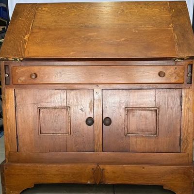 Rustic antique slant-top wooden desk featuring a upper drop-front writing surface, single drawer, and lower two-door cabinet with square...