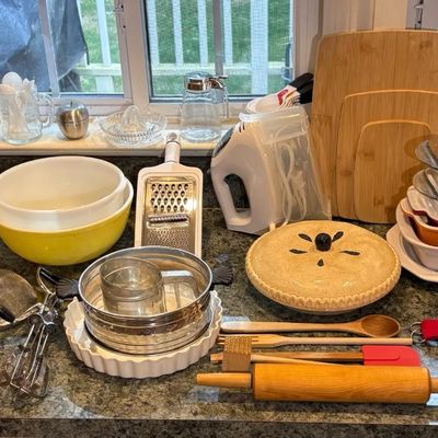 Assortment of modern and vintage kitchenware, including Pyrex mixing bowls and measuring cups, wooden cutting boards, baking dishes, and...
