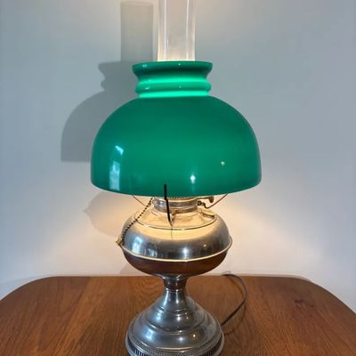 Vintage electrified oil lamp with a bright green cased glass banker-style shade, clear glass chimney, and metal base.
