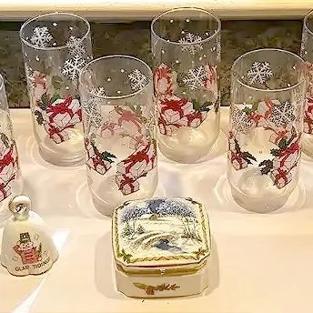 Collection of holiday decorations, including eight Christmas gift and snowflake highball glasses, a stained glass angel figurine, a glass...