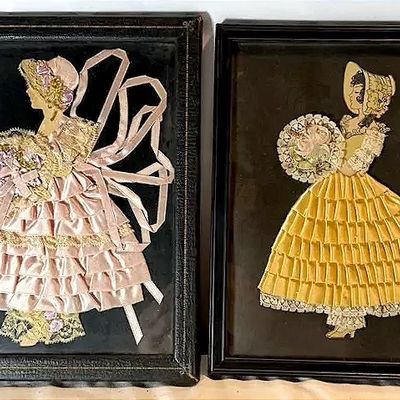 Pair of vintage framed ribbon art pictures featuring Southern belle figures in pink and yellow dresses with lace trim.