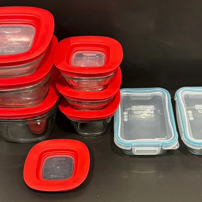 Collection of glass food storage containers, including Rubbermaid with red lids and Snapware with blue-rimmed locking lids.