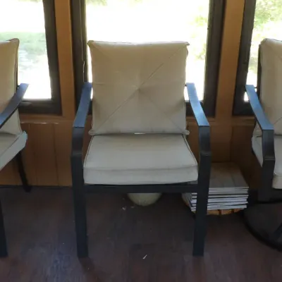 Set of three dark metal patio armchairs with beige fabric cushions, including two stationary armchairs and one swivel rocker chair.