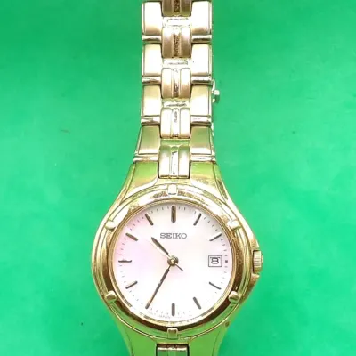 Women's gold-tone Seiko quartz wristwatch featuring a mother-of-pearl dial, date window, and link bracelet.
