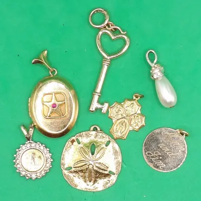 Collection of seven gold-tone pendants and charms, including an oval star-inset locket, heart-topped skeleton key, faux pearl teardrop,...