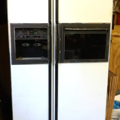 Vintage GE side-by-side refrigerator in white with black trim, featuring a door-front ice and water dispenser and a glass-front beverage...