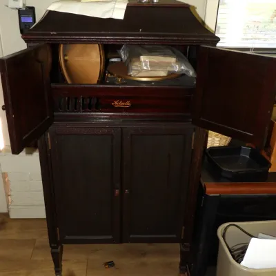 Vintage Pathé Actuelle floor-model phonograph in a dark wood cabinet, featuring a paper cone speaker and turntable behind upper double...