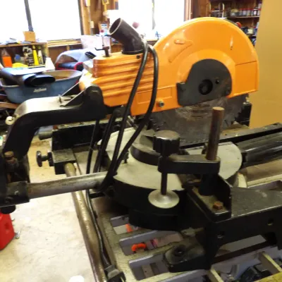 Heavy-duty electric sliding compound miter saw with an orange blade guard casing and integrated material clamp, showing typical signs of...