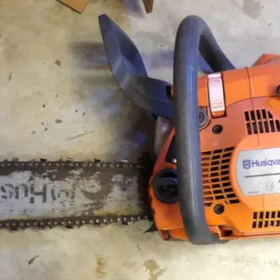 Husqvarna model 445 gas-powered chainsaw featuring an orange housing, top handle, and guide bar with attached chain.