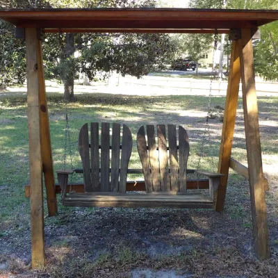 Freestanding wooden lawn swing featuring two Adirondack-style high-back seats suspended by metal chains under a covered A-frame canopy,...