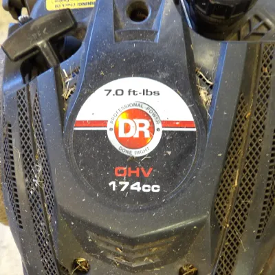 DR Power Equipment walk-behind lawn mower featuring a 174cc OHV engine with 7.0 ft-lbs gross torque, showing light dust and grass debris...