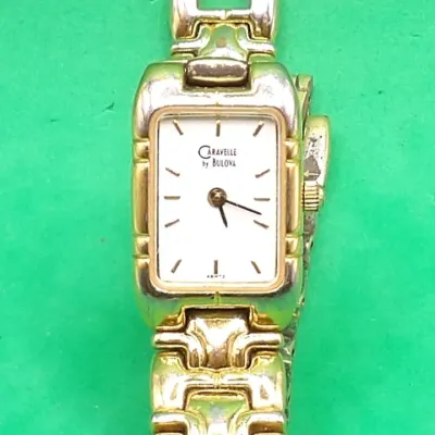Caravelle by Bulova women's gold-tone wristwatch featuring a rectangular white face with dash hour markers and an integrated...