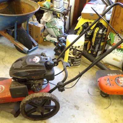 DR Power Equipment walk-behind field and brush mower alongside an orange DR walk-behind string trimmer and a Jackson wheelbarrow in a...