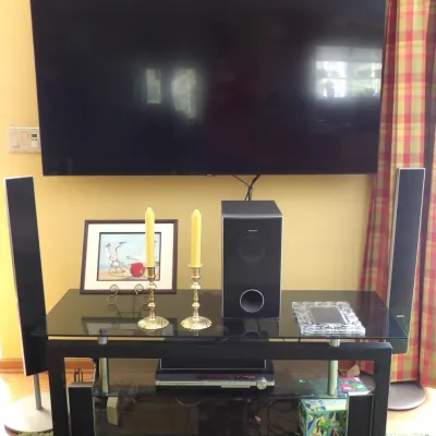 A wall-mounted flat-screen television positioned above a modern black glass TV stand housing a Sony surround sound speaker system, two...