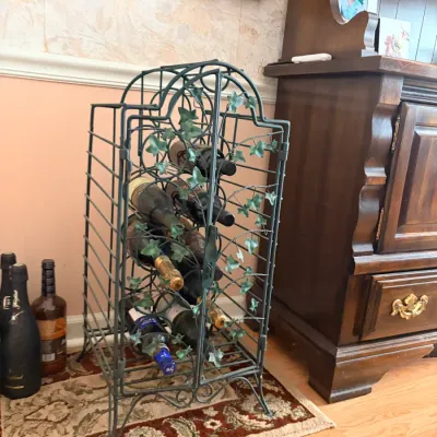 Vintage dark green wrought iron standing wine rack with faux ivy leaves, holding multiple wine and liquor bottles.
