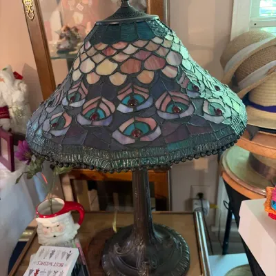 Tiffany-style table lamp featuring a stained glass shade with a peacock feather motif and a dark bronze finish base.