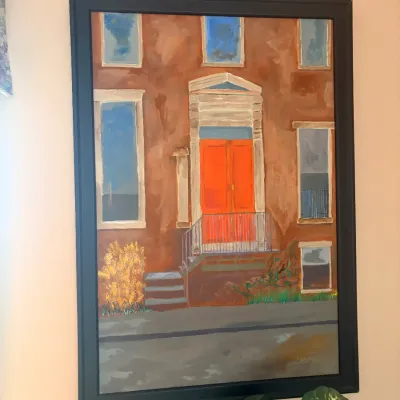 Framed acrylic on canvas painting depicting a brownstone building facade with bright orange doors, set in a sleek black frame.