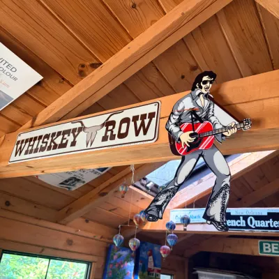 Novelty decorative items mounted on a wooden beam, featuring a longhorn 'Whiskey Row' metal sign and a cutout wall clock shaped...