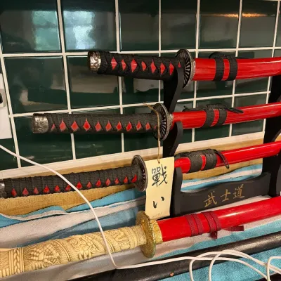 Set of three matching red-sheathed samurai sword replicas on a black display stand, alongside a sword featuring a faux-carved cream hilt.