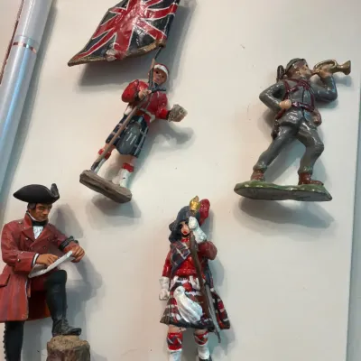 Sale Photo Thumbnail #127: Collection of four vintage hand-painted metal soldier figurines, including a British flag bearer in a kilt, a bugler, and a officer studying a map.