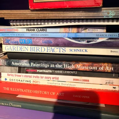 Sale Photo Thumbnail #144: Stack of art instruction, history, and reference books resting on a purple shelf beneath a vintage Swisher Sweets box.