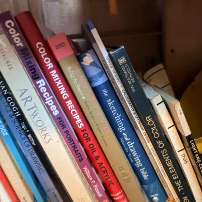 Sale Photo Thumbnail #153: Collection of art instruction and design books arranged on a wooden shelf, including titles on color mixing, drawing, and lettering.