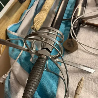 Collection of decorative swords and edged weapons, including a swept-hilt rapier with wire-wrapped grip, displayed alongside katana and...