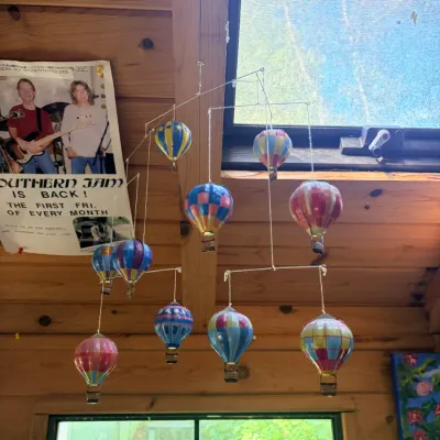 Hanging mobile featuring colorful mini hot air balloons with wire structures and woven baskets, suspended near a skylight.