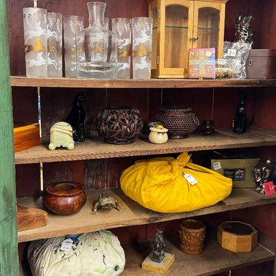 Sale Photo Thumbnail #30: Wooden display hutch filled with various collectibles including frosted glassware with gold horse motifs, small curio cabinets, woven baskets, and wrapped bundles.
