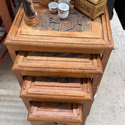 Sale Photo Thumbnail #19: Set of vintage carved wooden nesting tables featuring intricate Oriental relief scene tops, decorated with small collectables including carved horn statues and a sake set.