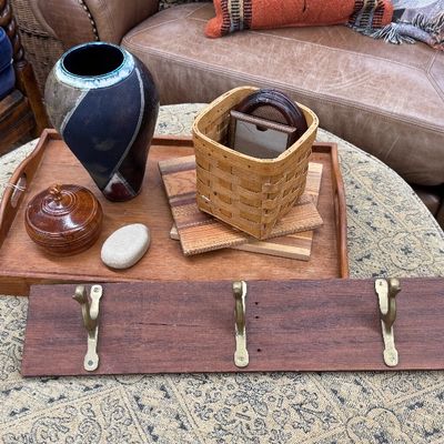 Sale Photo Thumbnail #10: Collection of home decor items displayed on an upholstered ottoman, including a wooden wall-mounted coat rack, a studio pottery vase, a lidded ceramic dish, a woven basket, and a wooden tray.