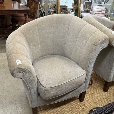 Upholstered channel-back barrel armchair with textured beige fabric and dark wooden legs.
