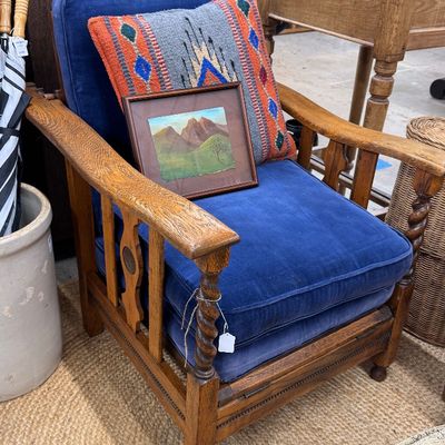 Sale Photo Thumbnail #7: Antique oak Morris-style armchair with blue velvet cushions, spiral-twist front posts, a framed landscape painting, and a Southwestern patterned accent pillow.