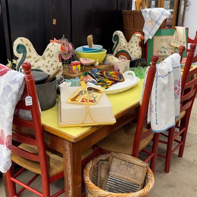Sale Photo Thumbnail #28: Rustic dining table set with red ladder-back chairs and woven seats, filled with various vintage kitchenware and home decor items.