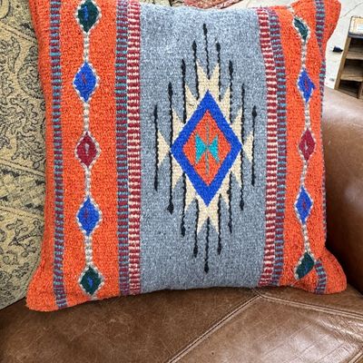 Southwestern-style woven throw pillow featuring vibrant orange, grey, and blue geometric patterns.