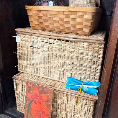 Collection of woven storage baskets including stacked wicker trunks, a rectangular wood-splint basket, and smaller natural fiber...
