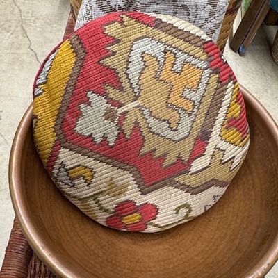Round kilim tapestry pillow resting inside a large copper basin, displayed on top of a woven wicker trunk.