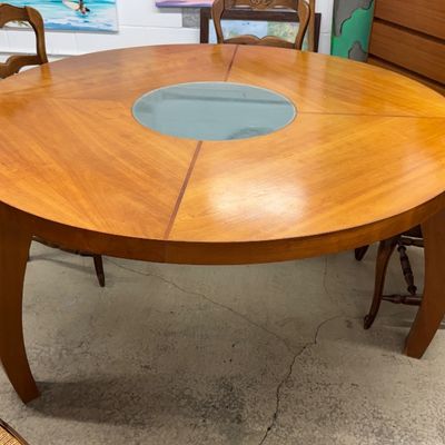 Round wood dining table featuring a segmented veneer top, inset glass lazy Susan center, and curved sabre legs.