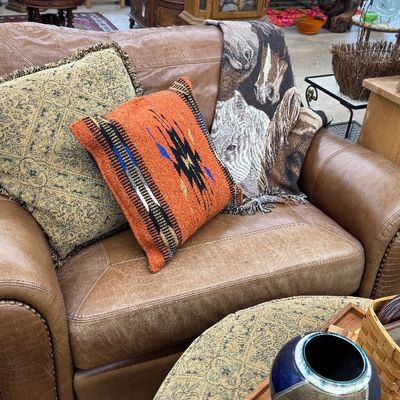Sale Photo Thumbnail #9: Rustic brown leather armchair with nailhead trim, styled with Southwestern pattern throw pillows and a woven horse blanket.