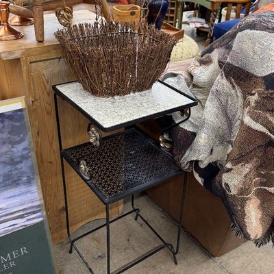 Sale Photo Thumbnail #15: Vintage wrought iron two-tier plant stand with a specked white top and ornate flower scroll details, topped with a rustic twig decorative basket.