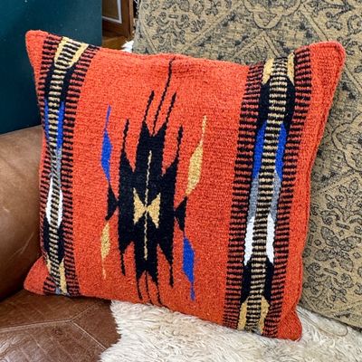 Southwestern-style woven wool throw pillow in vibrant orange with black, blue, and yellow geometric motifs.