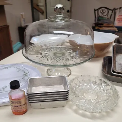Sale Photo Thumbnail #26: Vintage glass cake stand with dome lid, surrounded by various kitchenware items including aluminum mini loaf pans, Pyrex mixing bowls, and a vintage glass bowl.