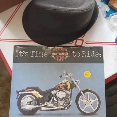 Sale Photo Thumbnail #36: Harley-Davidson 2005 16-month calendar alongside a dark grey felt trilby hat.