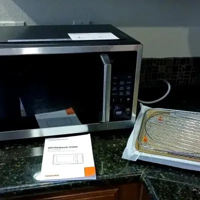 Modern Toshiba countertop microwave oven in black and stainless steel, accompanied by its instruction manual and wire roasting rack...