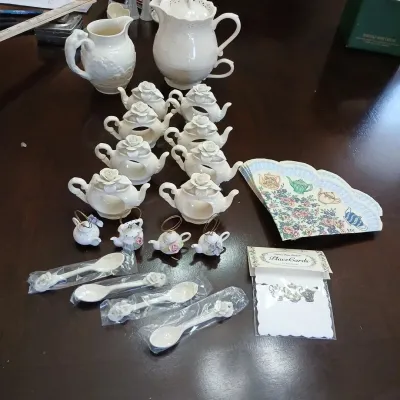 Collection of white ceramic tea accessories including teapot napkin rings, miniature teapot ornaments, ceramic spoons in original plastic...