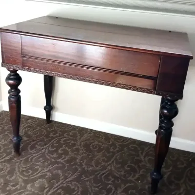Antique dark wood lift-top desk or console table featuring turned legs and carved trim detail along the apron.