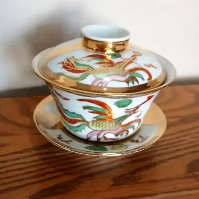 Chinese porcelain gaiwan tea set featuring hand-painted dragon and phoenix motifs with heavy gilt trim.