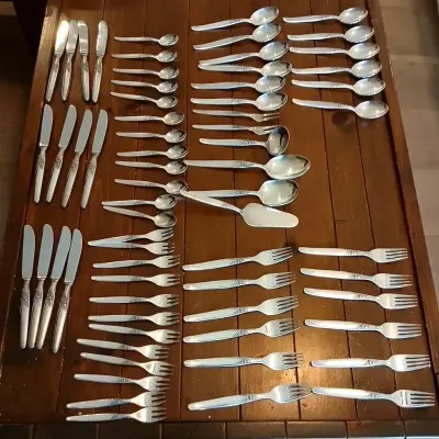 Large vintage silverplate flatware set arranged on a wooden table, featuring knives, forks, spoons, and serving pieces with etched floral...